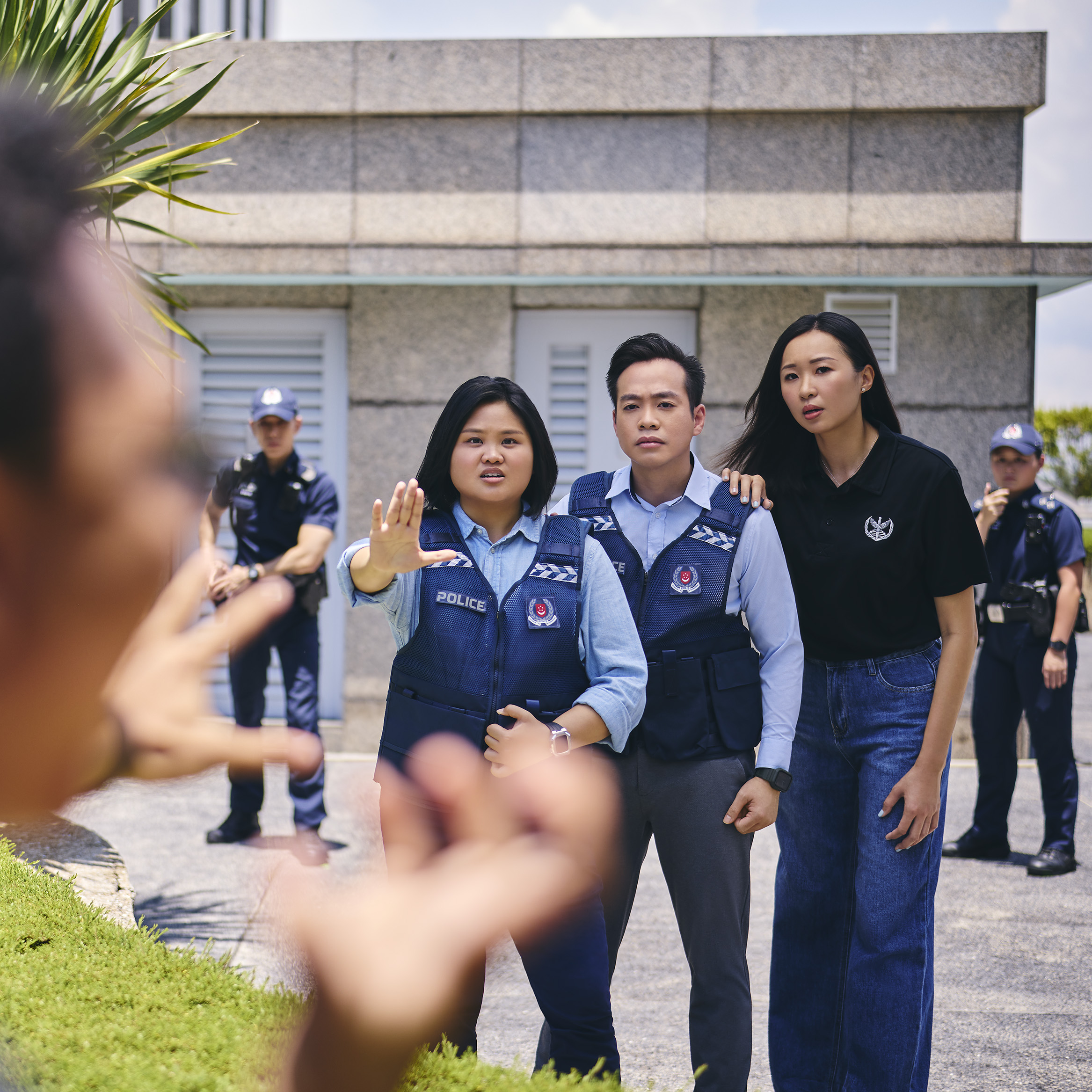 Three Singapore Police officers face forward, one with hand raised, stopping a blurry foreground person.